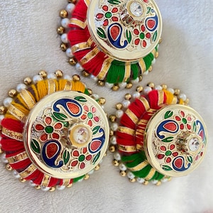 May include: Three circular decorative buttons featuring a gold-tone metal center with colorful enamel floral and paisley patterns and a central clear stone. The base is wrapped in red, green, and yellow thread with gold trim and white bead accents.