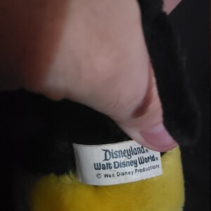 May include: Yellow plush toy with a black face and a white tag that reads "Disneyland Walt Disney World &copy; Walt Disney Productions".