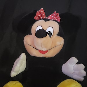 May include: A black and white plush toy of Minnie Mouse with a red bow with white polka dots. The toy has yellow feet and a white face with black eyes and a red mouth.