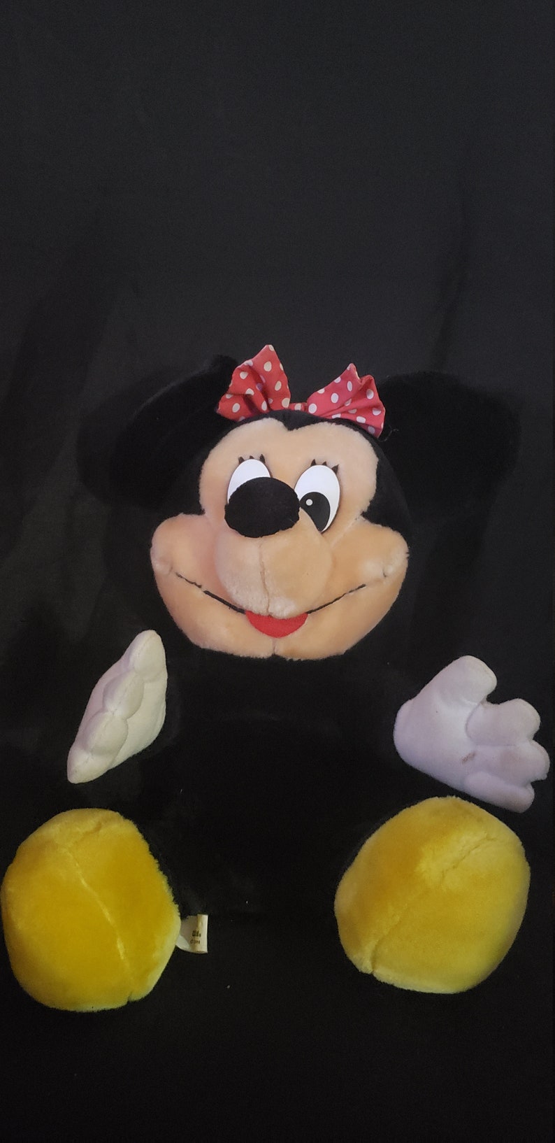 May include: A black and white plush toy of Minnie Mouse with a red bow with white polka dots. The toy has yellow feet and a white face with black eyes and a red mouth.