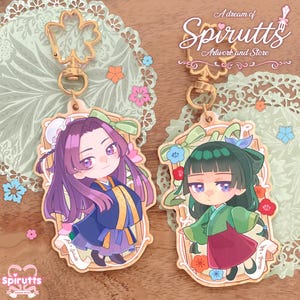 May include: Two anime-style keyrings featuring characters in traditional dress. One has a character with purple hair and a blue and gold outfit, the other has a character with green hair and a red and green outfit. Both have gold-coloured hardware and the text "A dream of Spirutts" is visible.
