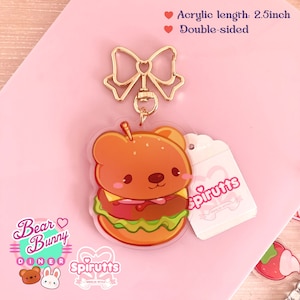 May include: A double-sided acrylic charm featuring a cartoon bear dressed as a hamburger. The charm is attached to a gold-coloured metal chain with a bow. The charm is 2.5 inches long and has the text "Spirutts" on it.