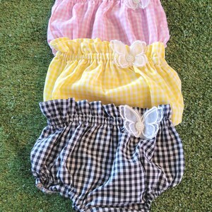 Può includere: Tre paia di bloomers a quadri con bordi arricciati e decorazioni a farfalla bianca. I bloomers sono rosa, gialli e bianco e nero.