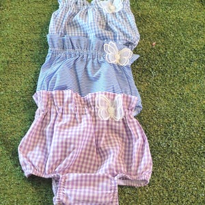 May include: Three layered baby bloomers with a gingham pattern in purple and blue. Each layer has a white butterfly applique.