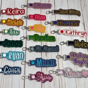 Puede incluir: Colecci&oacute;n de llaveros personalizados con nombres bordados en varios colores. Cada llavero tiene un cierre met&aacute;lico para facilitar su sujeci&oacute;n. Los nombres incluyen Keira, Ellanne, Jason Whiting, Eliza, Michele, Timothy, y otros.