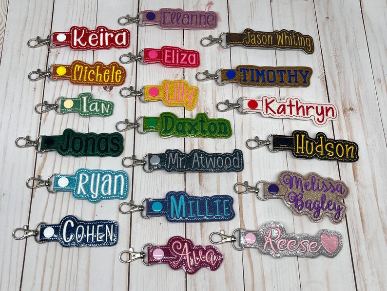 Puede incluir: Colecci&oacute;n de llaveros personalizados con nombres bordados en varios colores. Cada llavero tiene un cierre met&aacute;lico para facilitar su sujeci&oacute;n. Los nombres incluyen Keira, Ellanne, Jason Whiting, Eliza, Michele, Timothy, y otros.