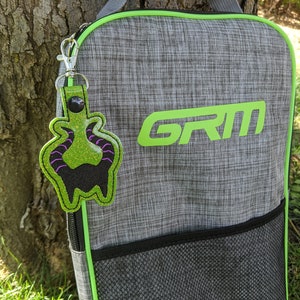 May include: A gray and green sports bag with a black mesh pocket and a green zipper. The bag has the word "GRIM" printed on the front in green letters. A green and purple monster keychain is attached to the bag.