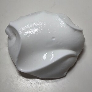 May include: A close-up of a white, fluffy slime. The slime is smooth and glossy, with a slightly textured surface.