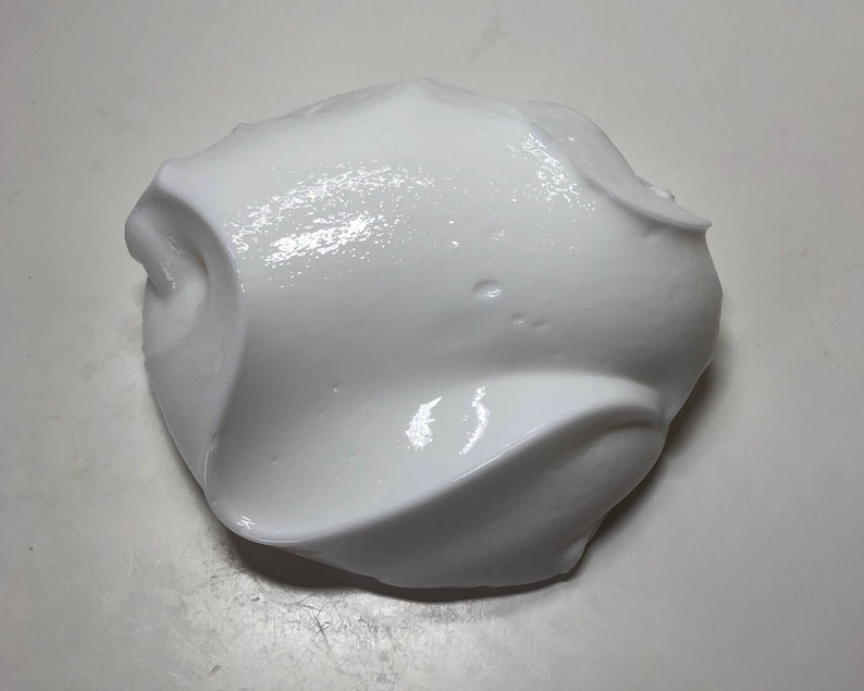 May include: A close-up of a white, fluffy slime. The slime is smooth and glossy, with a slightly textured surface.