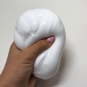 May include: A close-up of a white slime being held in a hand. The slime is soft and gooey, and it has a smooth, glossy surface.