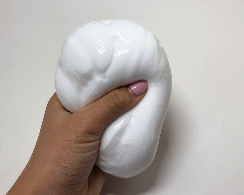 May include: A close-up of a white slime being held in a hand. The slime is soft and gooey, and it has a smooth, glossy surface.