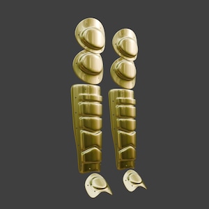 May include: A pair of gold-colored metallic shin guards and knee protectors. Each set consists of a multi-segmented lower leg piece with horizontal ridges, two rounded knee plates, and a small curved foot guard at the bottom of each unit.