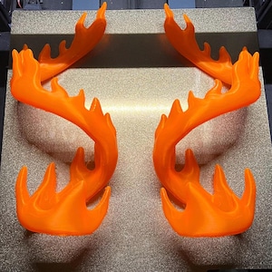 May include: Four bright orange, flame-shaped decorative pieces. Each piece has a curved design with multiple pointed tips, resembling stylized flames. The objects are arranged in pairs, suggesting they are meant to be used together, possibly as a decorative element.