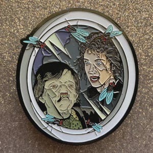 May include: Enamel pin featuring a scene with two characters and several flies. The pin has a silver border with a white and gray interior. The characters have a distressed appearance, with one appearing to be transforming. The flies are light blue with red accents.