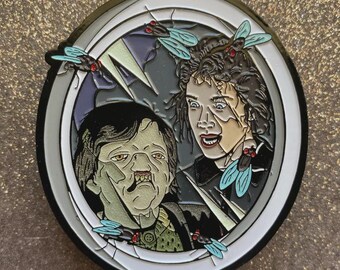 May include: Enamel pin featuring a scene with two characters and several flies. The pin has a silver border with a white and gray interior. The characters have a distressed appearance, with one appearing to be transforming. The flies are light blue with red accents.