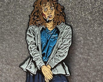 May include: Enamel pin depicting a woman with messy brown hair, wearing a white jacket over a blue shirt and a dark blue skirt. She has a cigarette in her mouth and a weary expression. The pin is set against a gray background.