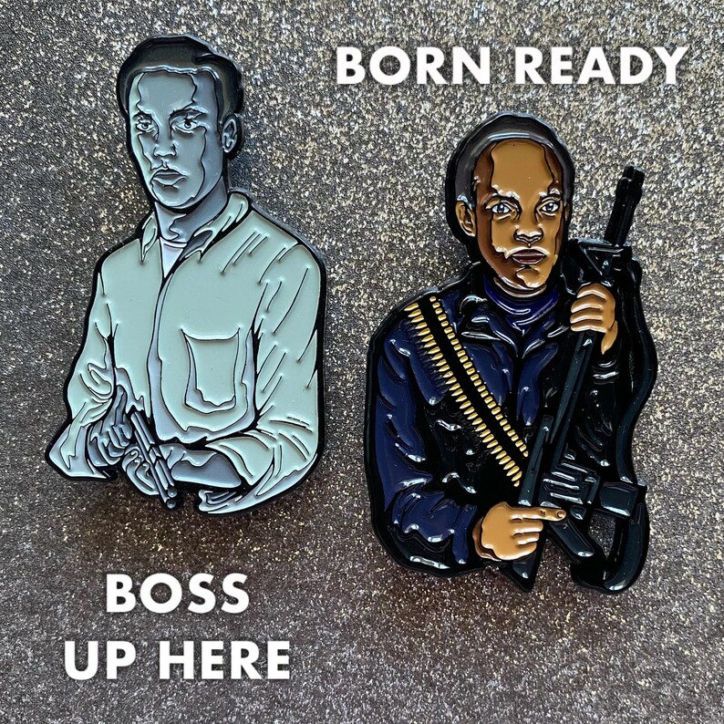 Op de afbeelding: Twee emaillepins met een zwarte man. De pin aan de linkerkant toont een man in een lichtblauw shirt die een pistool vasthoudt. De tekst "BOSS UP HERE" staat onder de pin. De pin aan de rechterkant toont een man in een donkerblauw jack die een geweer vasthoudt. De tekst "BORN READY" staat boven de pin.