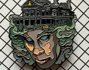 May include: A detailed enamel pin featuring a haunted house design atop a stylized face with blue eyes. The house is black with yellow accents, and the face has gray, brown, and orange tones. Green smoke-like elements surround the face.