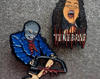 Könnte beinhalten: Zwei Emaille-Pins, die Charaktere aus dem Horrorfilm 'The Texas Chainsaw Massacre' darstellen. Der erste Pin zeigt eine Frau mit langen braunen Haaren, einem rot-weiß gestreiften Hemd und einem blutigen Mund. Der zweite Pin zeigt einen Mann in einer blauen Jacke, der eine Kettensäge hält und einen blutigen Arm abschneidet. Der Text 'The Texas Chainsaw Massacre' ist auf dem ersten Pin geschrieben.
