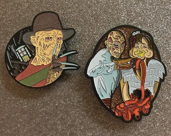 May include: Two enamel pins featuring Freddy Krueger from the Nightmare on Elm Street films. One pin shows Freddy with his clawed glove, the other depicts a scene from the movie. The pins have black borders.