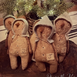 May include: Four tan fabric snowman dolls with stitched facial features and brown noses. Each doll wears a light gray hood tied with string and features a small square patch on the chest with the letter J embroidered in black thread.