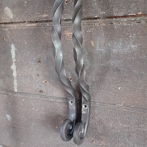 May include: Two black metal door handles with a twisted design. The handles are attached to a wooden surface with screws.