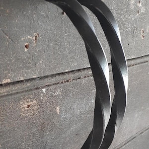 May include: Two black metal twisted handles with a silver screw in each. The handles are mounted on a wooden surface.