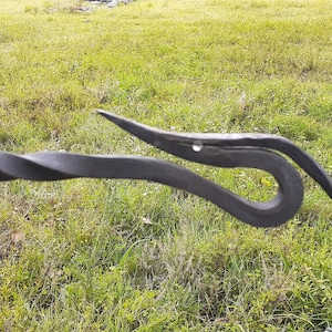 May include: A black metal gate latch with a twisted rod and a decorative loop at the end.