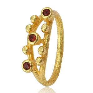 May include: A gold ring with a delicate design featuring a row of small beads and three red gemstones.