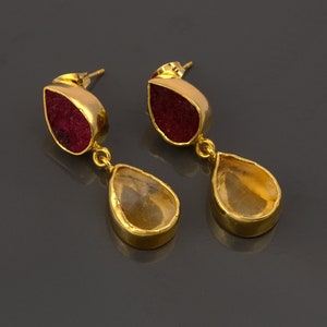 May include: Gold dangle earrings with a teardrop-shaped red gemstone on top and a teardrop-shaped clear yellow gemstone on the bottom.