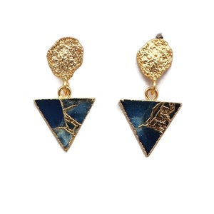 May include: Gold-tone earrings with a textured top and a triangular pendant. The pendant has a dark blue and gold-veined pattern. The earrings are suspended against a white backdrop.