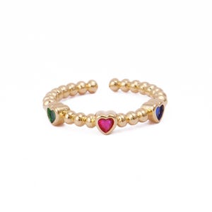 May include: Gold ring with a beaded band and three heart-shaped stones. The stones are red, green, and blue.