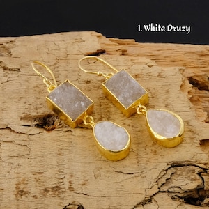 Puede incluir: Un par de pendientes de tono dorado con gotas de piedra druzy blanca. Los pendientes presentan una piedra rectangular en la parte superior y una piedra en forma de lágrima en la parte inferior.