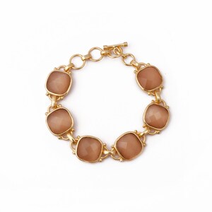 Op de afbeelding: Een gouden armband met een schuifgesp en zes vierkante bruine stenen.