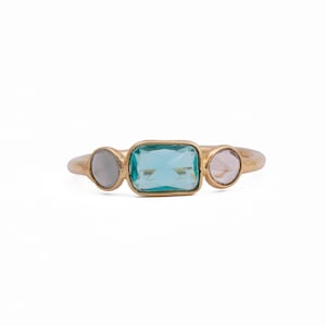 Puede incluir: Anillo de oro con tres piedras preciosas: una piedra blanca redonda, una piedra azul rectangular y una piedra rosa redonda.