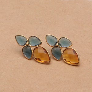 May include: A pair of gold tone earrings with blue and amber colored glass stones. The stones are shaped like leaves and are arranged in a flower-like pattern.