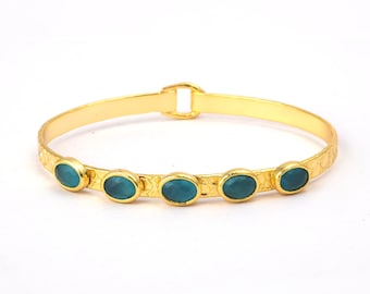 May include: A gold bangle bracelet with five oval-shaped turquoise gemstones set into the band.