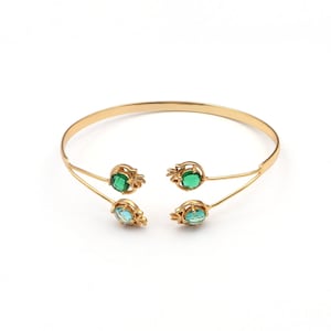 May include: A gold bangle bracelet with two green and two blue gemstones. The gemstones are set in a floral design.