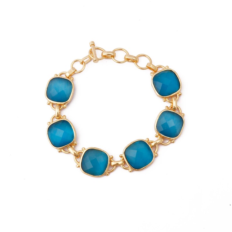Op de afbeelding: Een gouden armband met zes blauwe edelsteen schakels. De armband heeft een karabijn sluiting.
