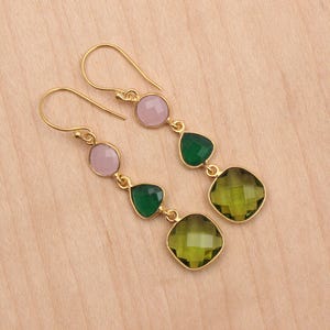 May include: Gold dangle earrings with three gemstone drops. The top drop is pink, the middle two are green, and the bottom drop is a larger, square-shaped green gemstone.