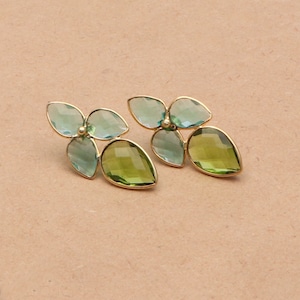 Puede incluir: Un par de pendientes de tono dorado con detalles de piedras preciosas verdes y azules. Los pendientes presentan un diseño floral con múltiples piedras en forma de lágrima.