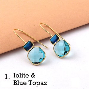 May include: Gold dangle earrings with a light blue square gemstone and a smaller dark blue square gemstone. The earrings are labeled "1. Iolite & Blue Topaz".