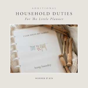 May include: A white planner with a ring binding and a page that says "I can serve my family" with an illustration of clothes hanging on a clothesline. The text "hang laundry" is below the illustration. The planner is on a white surface with wooden clothespins.