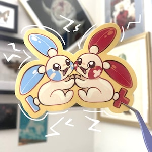 May include: A sticker featuring two cartoon characters, one blue and one red, with a yellow background. The characters are holding hands and smiling. The sticker has a white outline and is surrounded by white lightning bolts.