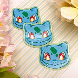 May include: Three blue and green cartoon character stickers with red eyes. The stickers are on a striped background.