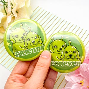 May include: Two green round buttons with alien dog illustrations. One button says "FRIENDS" and the other says "FOREVER". The buttons are on a striped background with flowers.