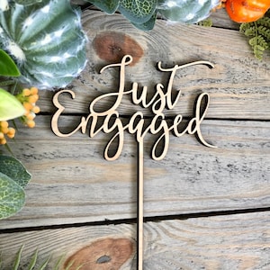 May include: Wooden cake topper with the words "Just Engaged" in a cursive font.