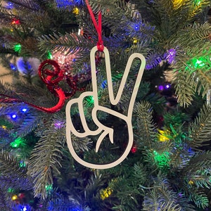 May include: White peace sign ornament hanging on a Christmas tree with colorful lights.