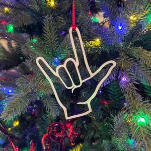 May include: White ornament shaped like the American Sign Language symbol for "I love you". The ornament is hanging on a Christmas tree with colorful lights.