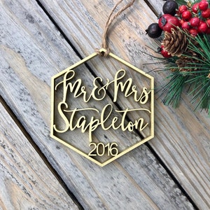 May include: Gold hexagonal Christmas ornament with the text "Mr & Mrs Stapleton 2016" in a cursive font.